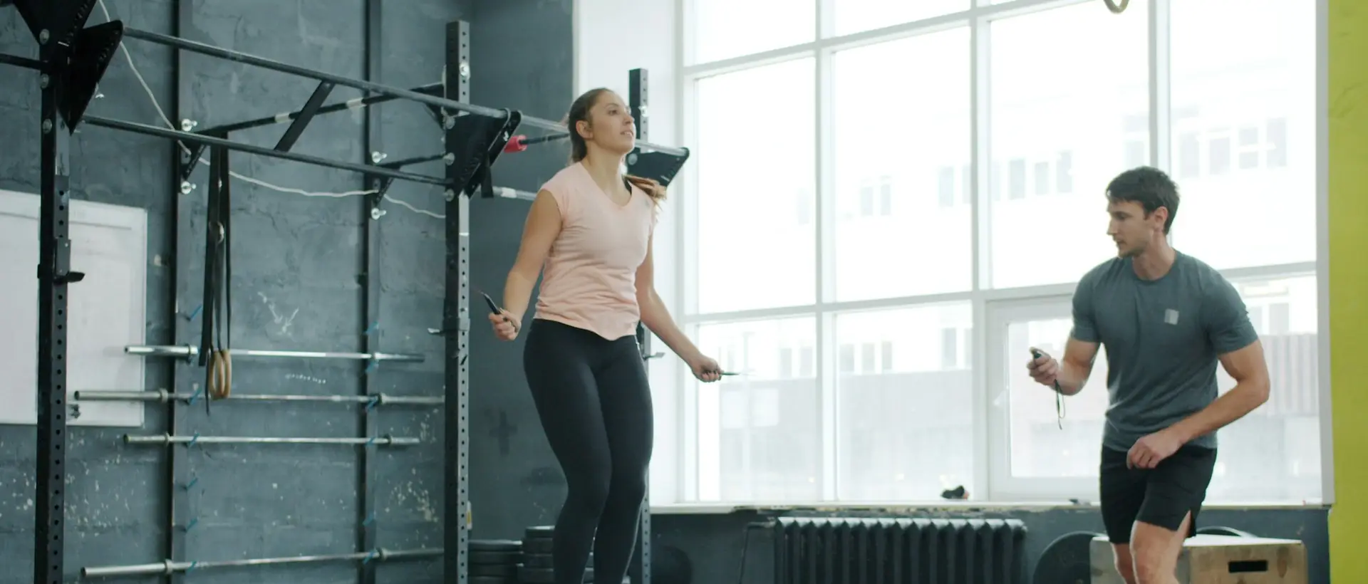 A woman jumping rope in a bright gym while a coach watches