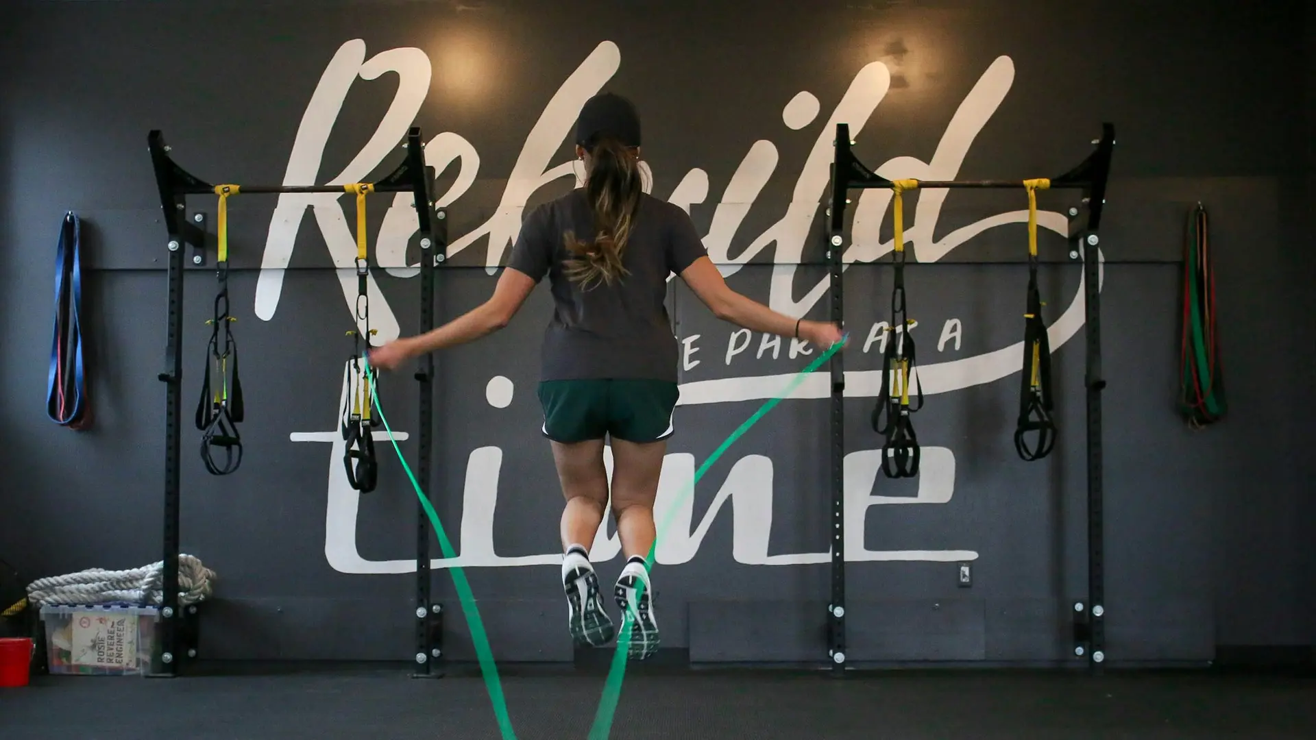 A woman skipping with a green jump rope in a dark training room